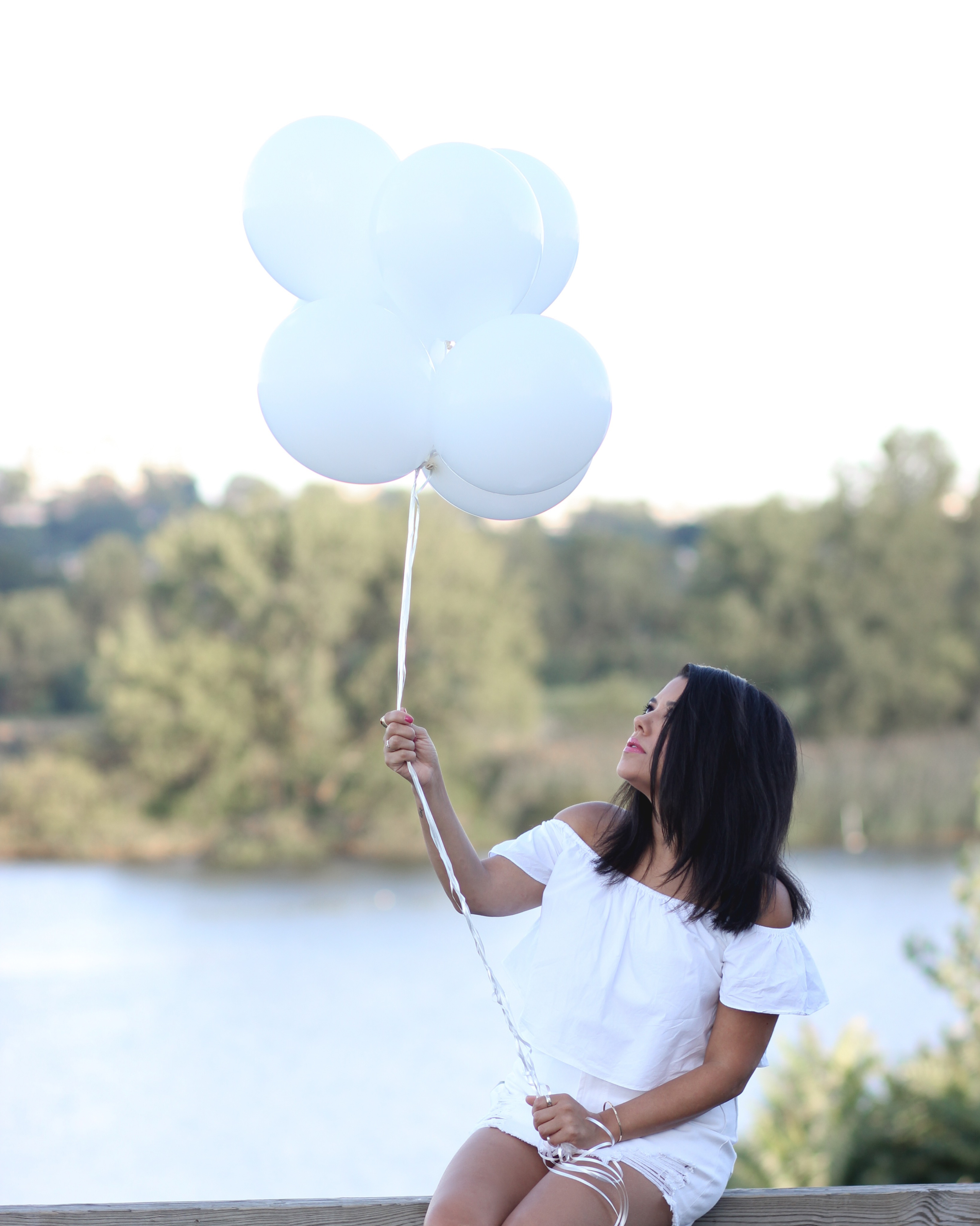 lifestyle blogger naty michele sitting down wearing all white holding white balloons
