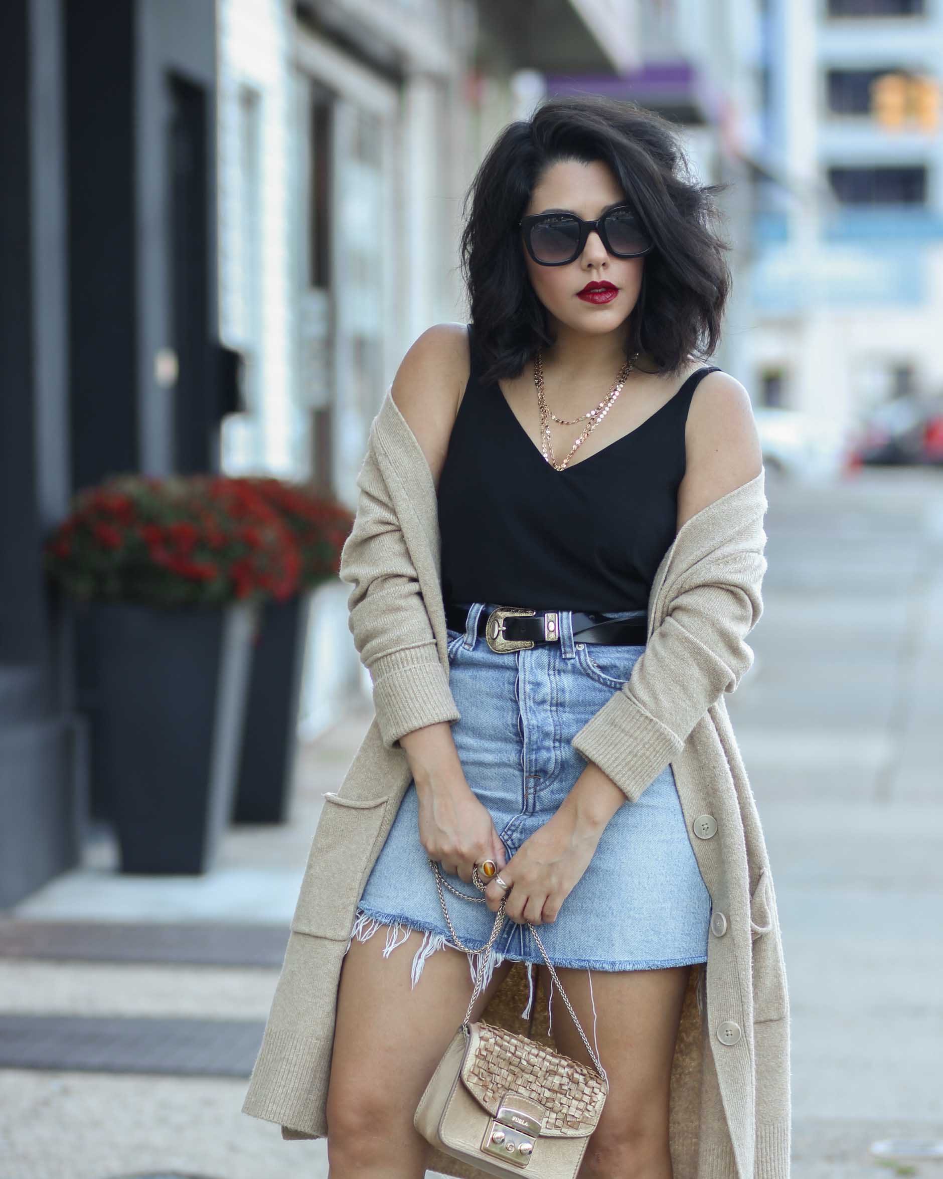 close up of style blogger naty michele wearing a denim skirt with a belt and oversized cardigan 
