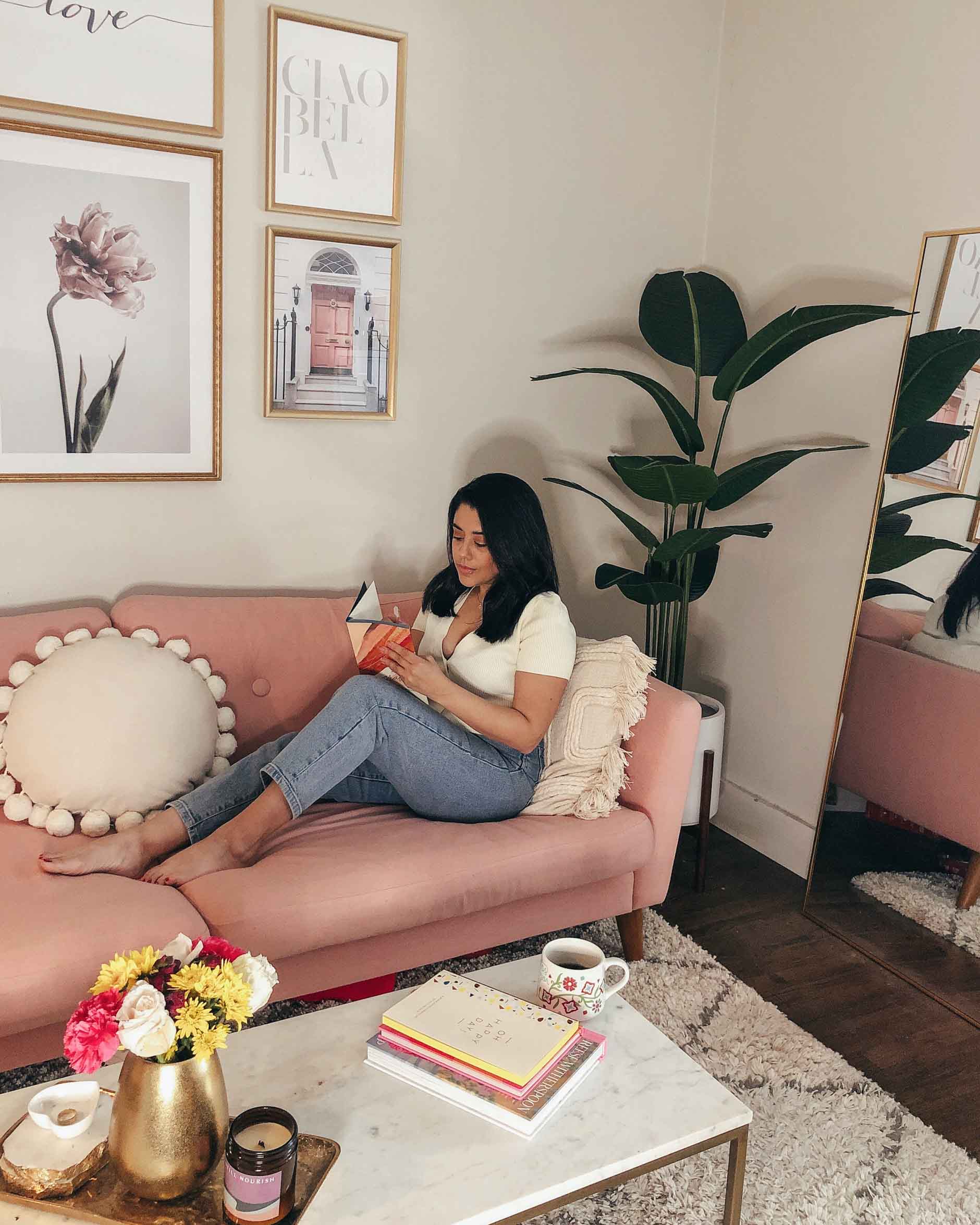 living room decor with a faux plant and large gold mirror, naty michele is on the sofa journaling