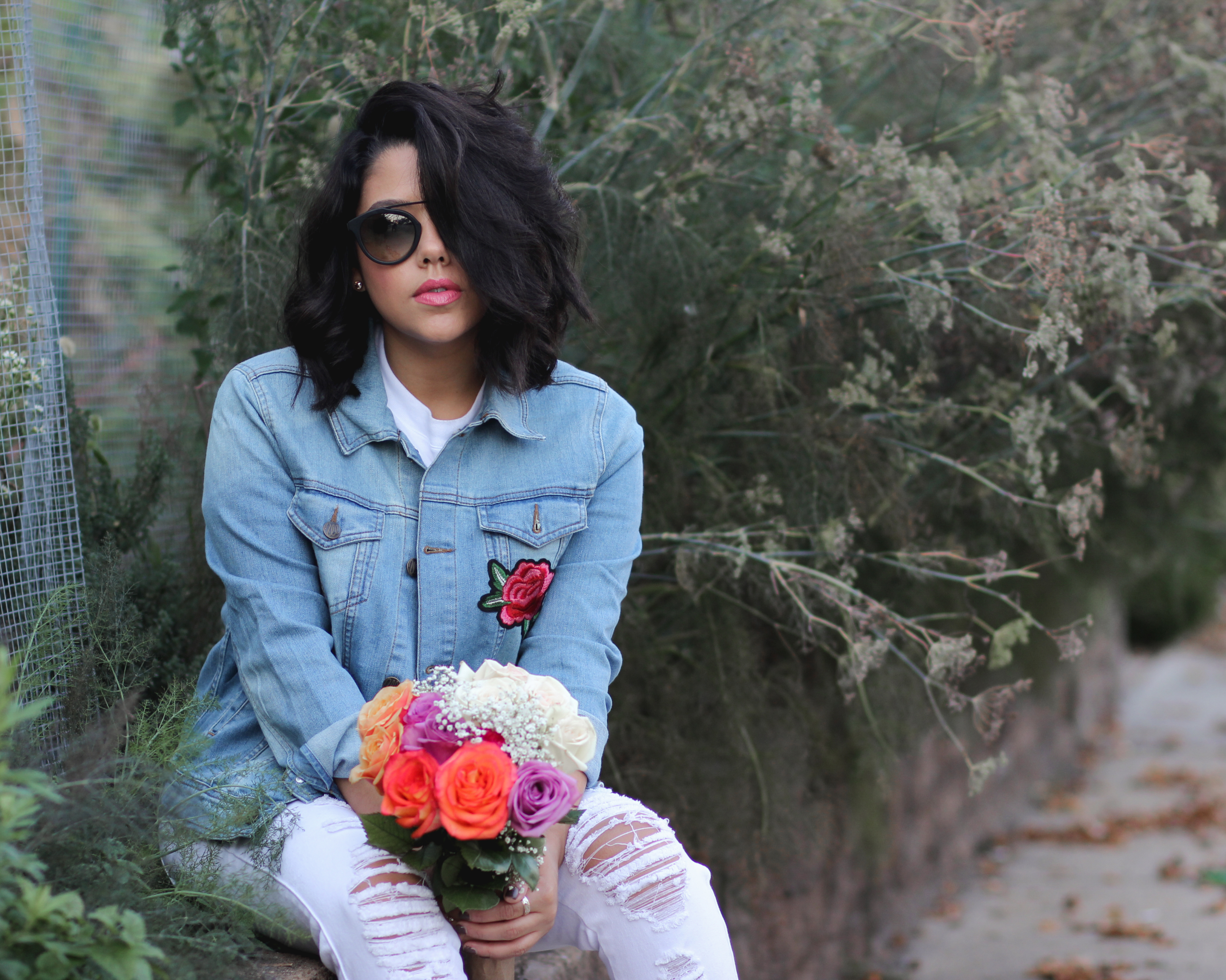 lifestyle blogger naty michele sitting down holding roses wearing a denim jacket