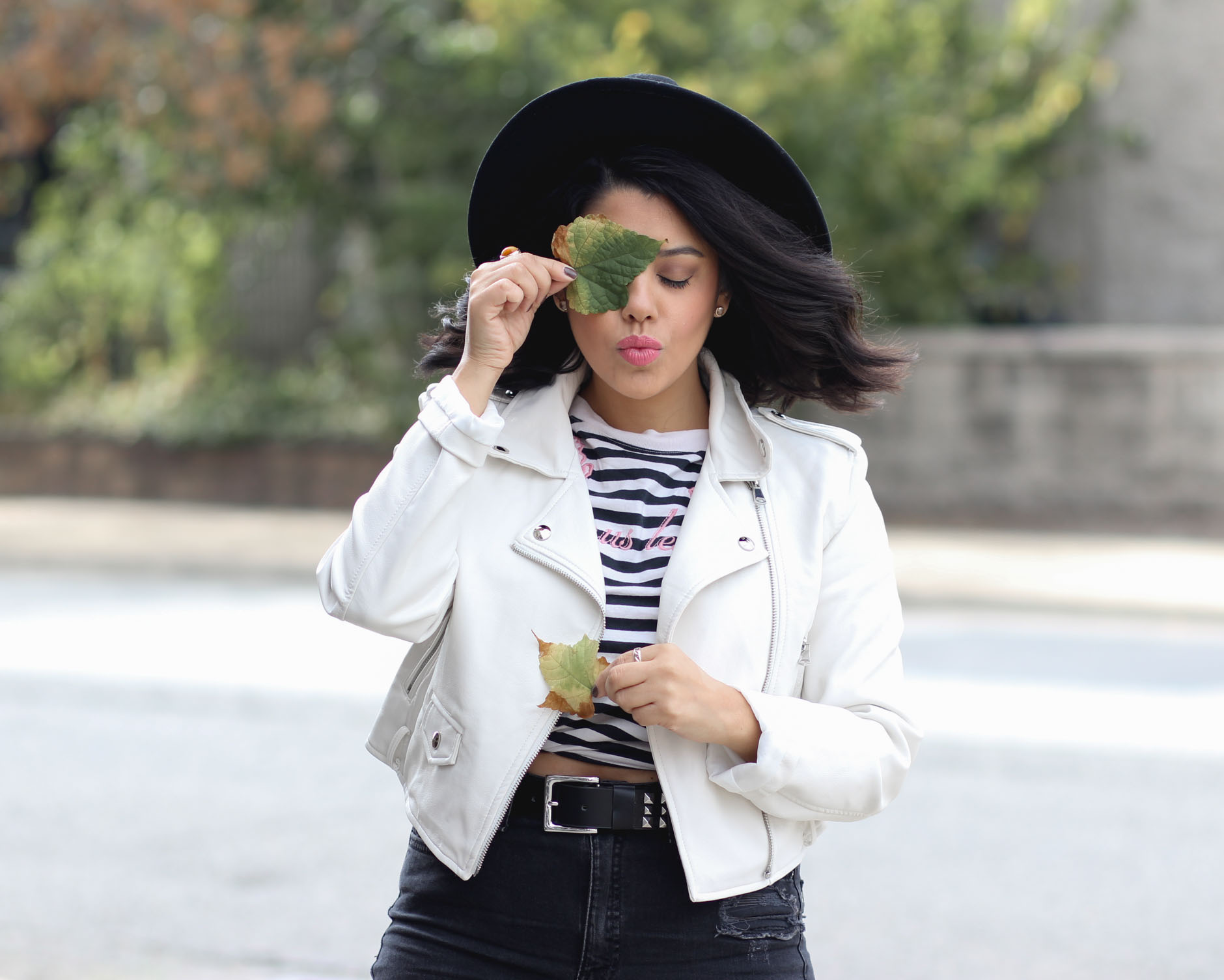 lifestyle blogger naty michele wearing a faux leather jacket and holding up a leaf