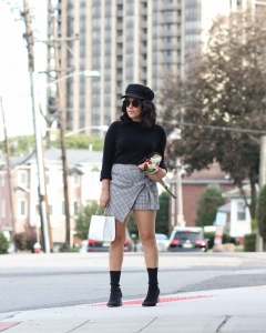 lifestyle blogger naty michele holding flowers wearing a plaid skort and sock boots